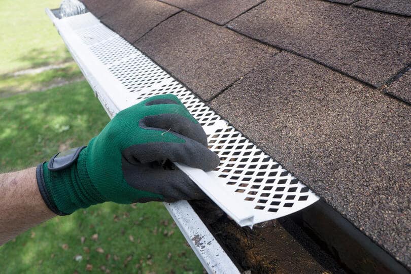 leaf filter gutters-gloved hand installing white gutter guards to gutter system
