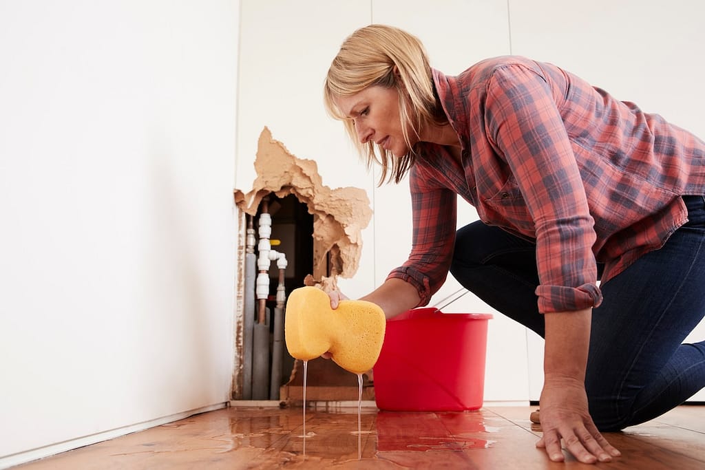 emergency plumbing Worried woman mopping up water from a burst pipe with sponge