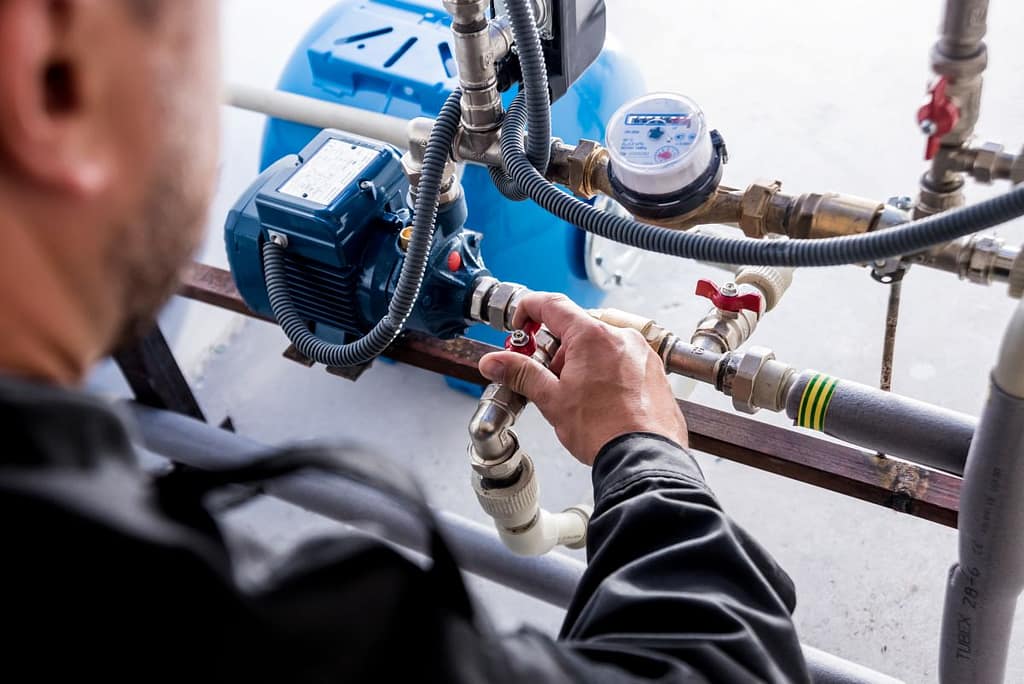 backflow testing technician repairing and adjusting water pipes outside of family house