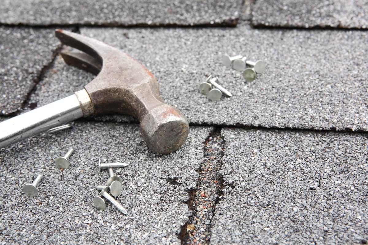Hammer and nails on damaged roofing shingles