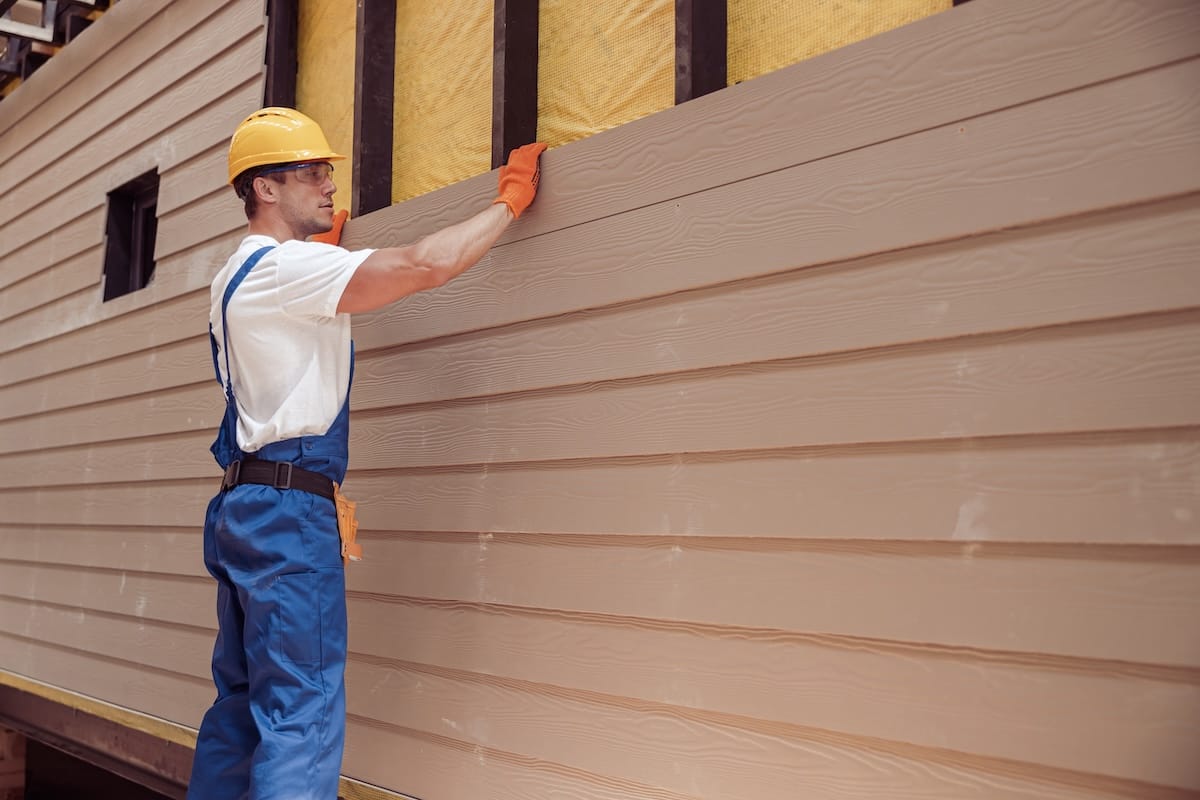 Worker installing composite siding that resembles wood texture