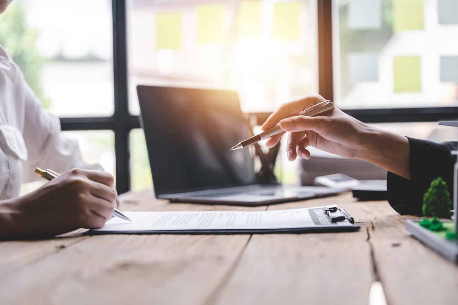 how to file a roof insurance claim close up view of two people's hands reviewing a homeowners insurance policy with paper and a laptop