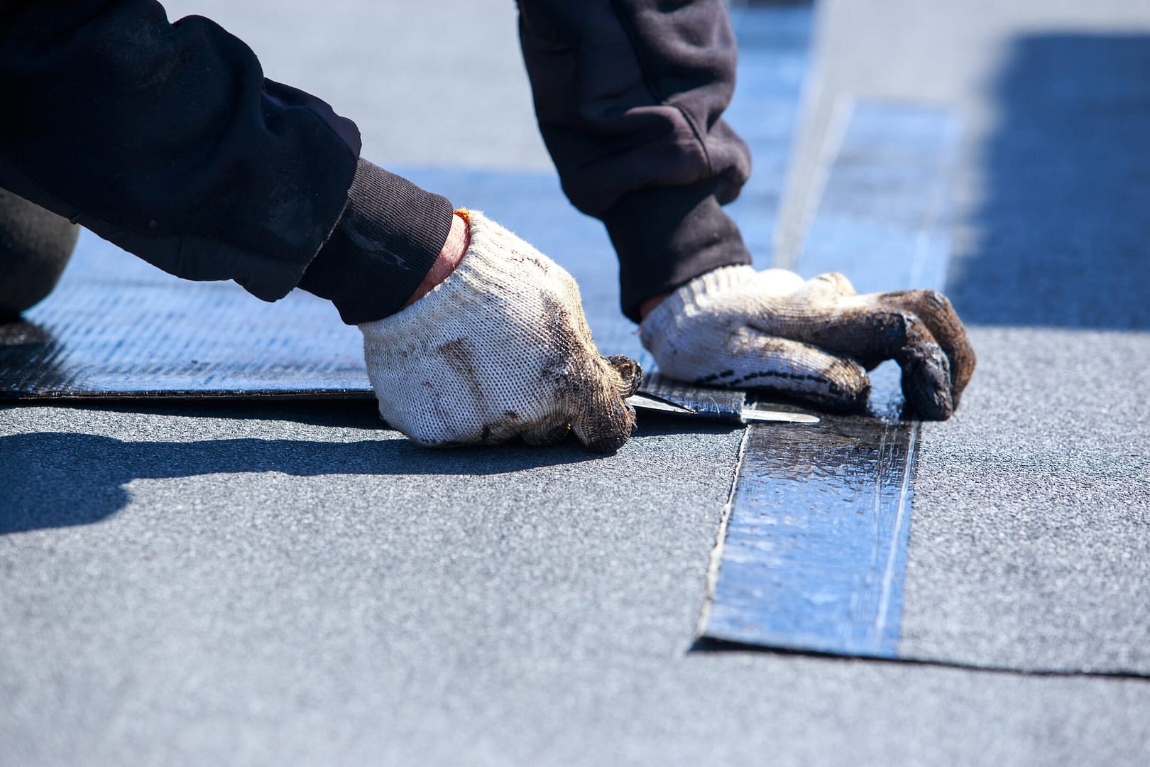 flat roof repair-close up of gloved tech installing new section of flat roofing materials