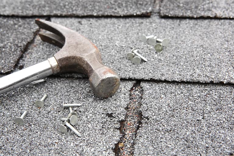 Hammer and nails on damaged roofing shingles