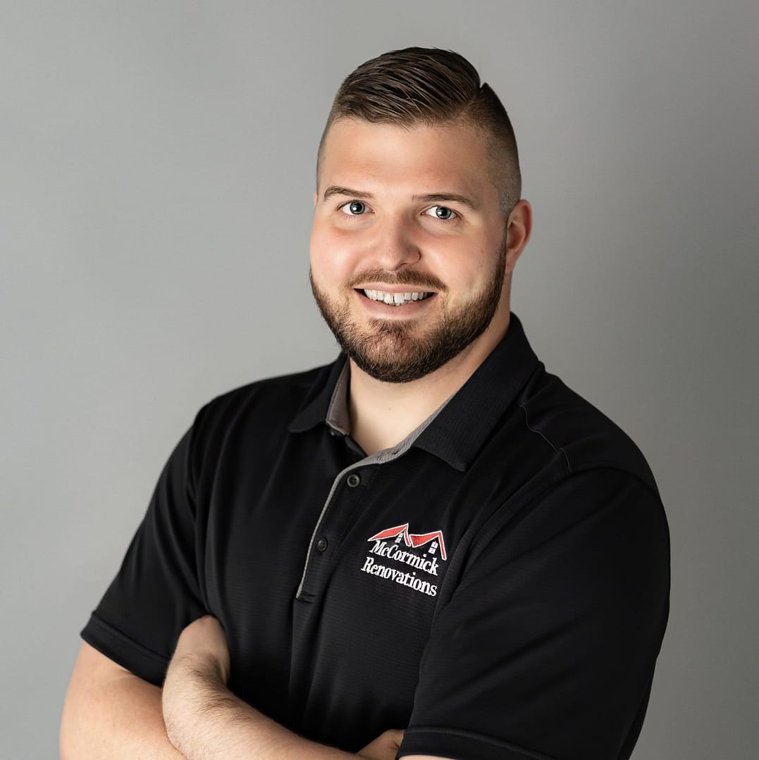 A man with a beard and short hair, smiling and dressed in a black polo shirt with a logo that reads "Kentarnick Renovations," stands against a gray background, arms crossed in a confident pose.