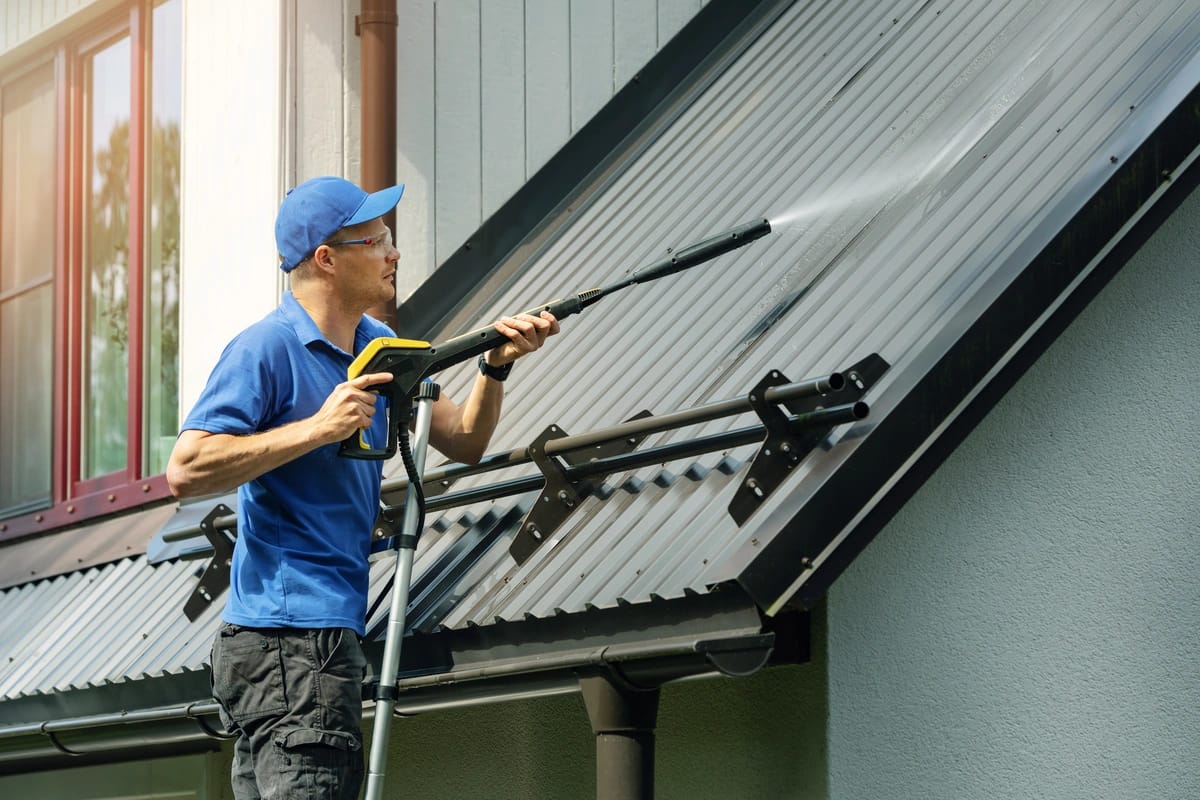 A roofer powerwashes a metal roof