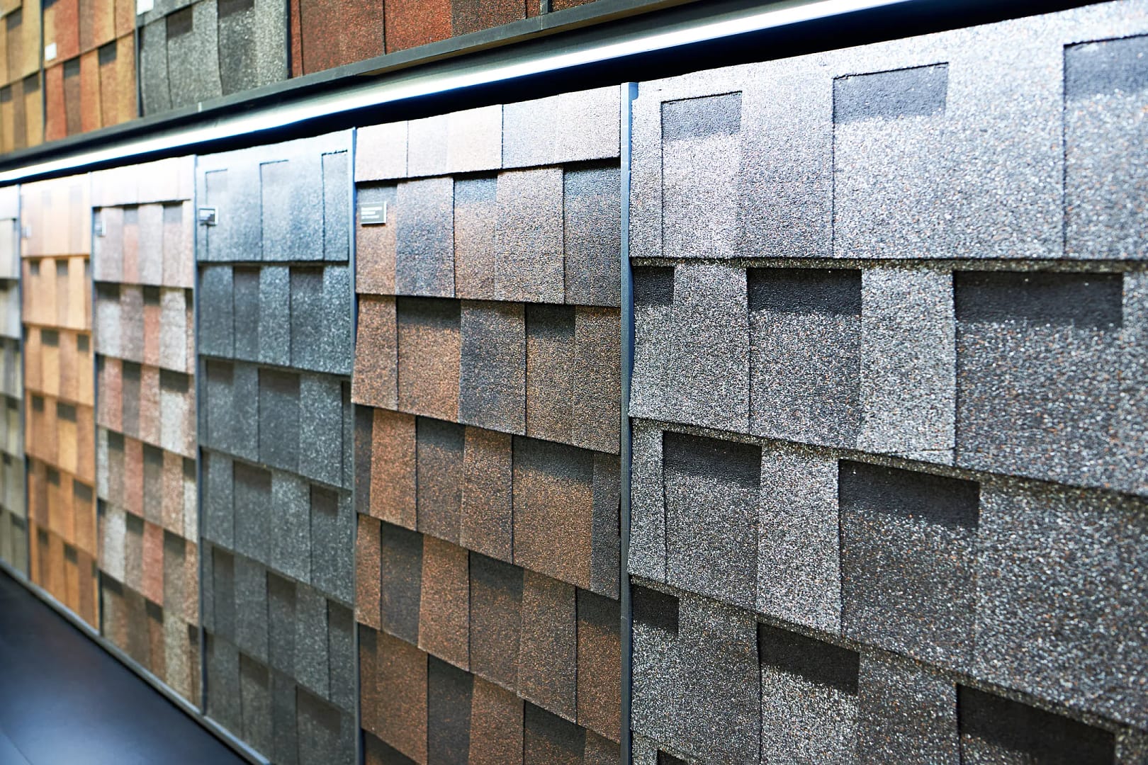 A display of the best roofing shingles showcases a variety of colors and textures, featuring shades of gray, brown, and red, all elegantly arranged in a well-lit showroom.