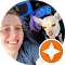 A person smiles while sitting next to a small dog with its tongue out. Both are in a car. The photo is framed with a circular border, and a star icon is visible in the bottom right corner.