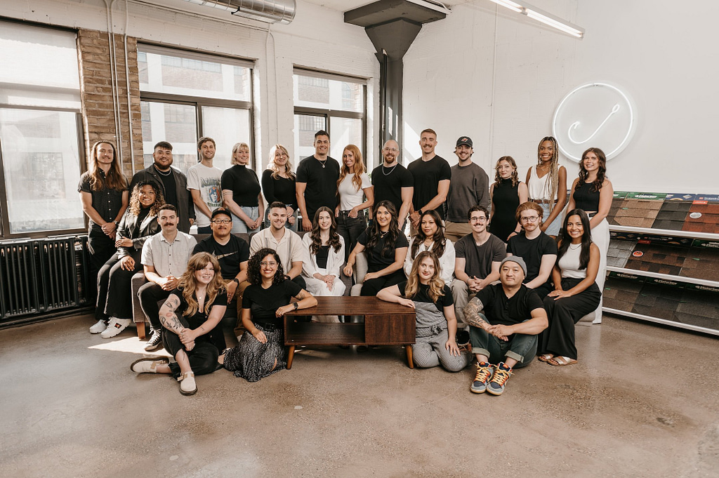 On our website, you'll find a photo of the dynamic Hook Agency team in a bright, modern space with large windows and a glowing sign. Gathered around a large wooden table, their smiles capture the essence of unity that drives us forward.