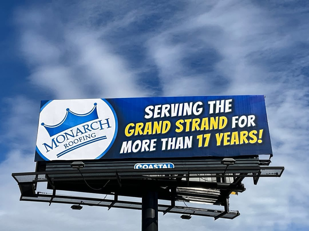 A billboard set against a cloudy sky prominently features Monarch Roofing's crown logo and states, "Proudly serving the Grand Strand for over 17 years.