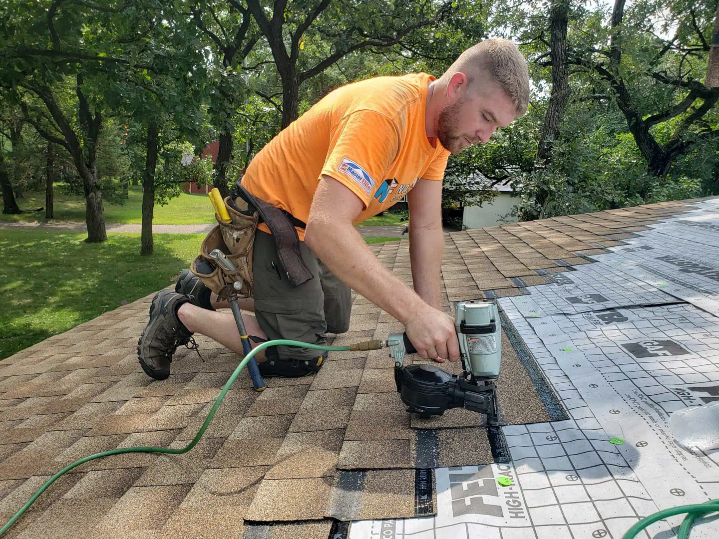 On a Minneapolis rooftop, beneath towering trees, a man in a bright orange shirt expertly uses a nail gun to install shingles. His precise and skillful approach mirrors the meticulous nature of our PPC campaigns at Hook Agency.