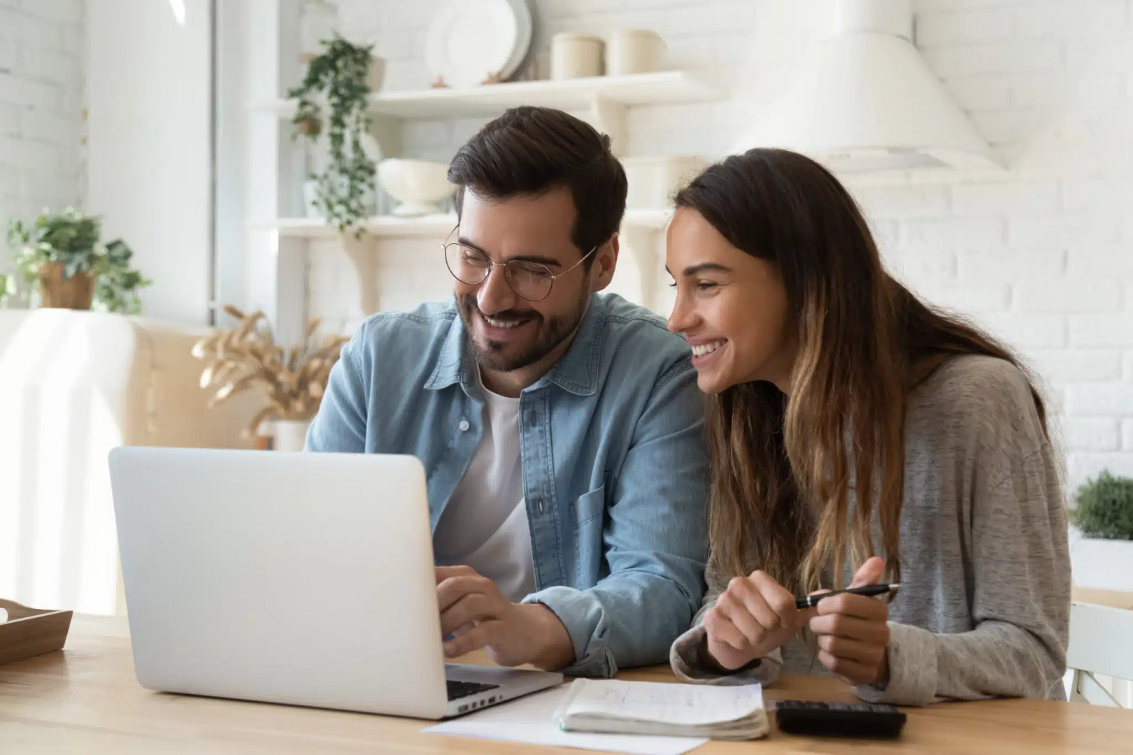 A man and woman sit at a table, intently reviewing Fargo SEO strategies on a laptop. They appear engaged and satisfied, with notebooks and a pen ready for action in the bright, modern setting.