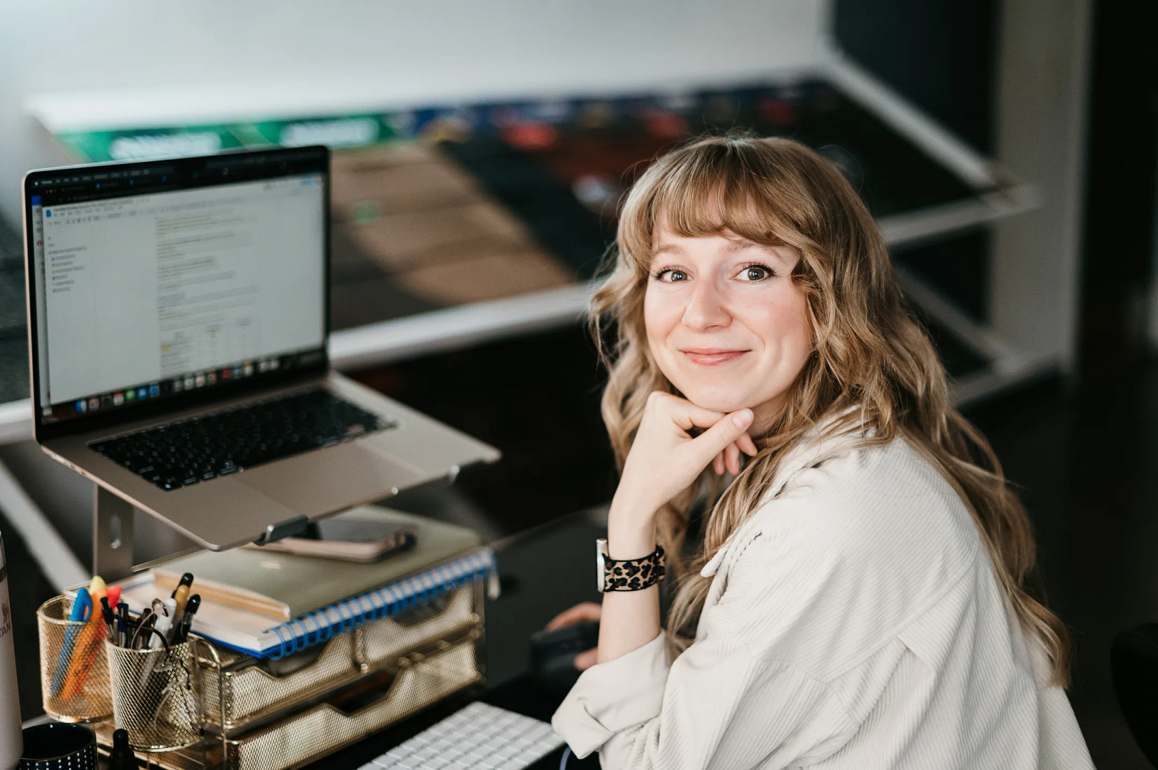 A person with long blonde hair sits confidently at a desk, smiling at the camera. Engaged in content marketing strategy, they have an open laptop nearby, accompanied by office supplies and a paper organizer.