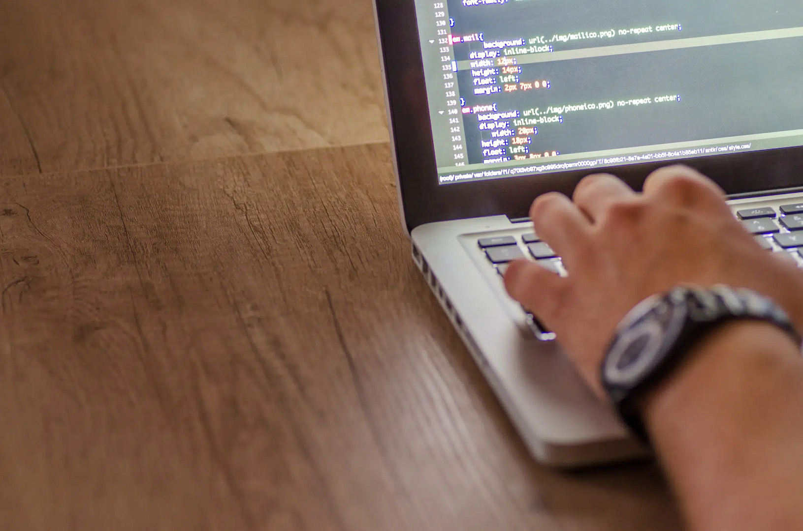 A person types code on a laptop placed on a wooden table, illustrating active engagement in software development—potentially creating cutting-edge solutions for Salt Lake City's flourishing web design community.