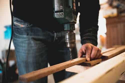 On Hook Agency's website, a tradesman, donning jeans and a black sweater, demonstrates expert craftsmanship by efficiently drilling precise holes into wooden planks.