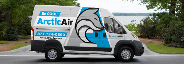 A white Arctic Air HVAC van wrap, prominently displaying a bold blue and gray dolphin logo, contact number, and website, is parked roadside with trees and a lake in the background.