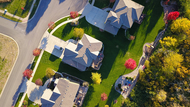 Eagleview presents a stunning aerial perspective of a suburban neighborhood, showcasing four homes with gray roofs nestled among vibrant green lawns and autumn-colored trees. The image highlights curved roads, driveways, and a landscaped garden in the bottom right corner.