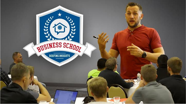 A speaker in a red shirt addresses an audience at Roofing Insights' Business School, as attendees actively engage with laptops poised for an insightful session.