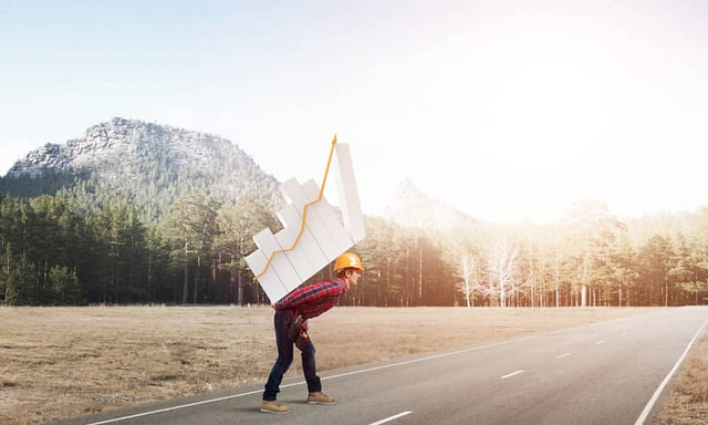 A hard-hatted individual in a plaid shirt strides confidently along a road, carrying an upward-trending graph. Trees and mountains rise under a bright sky, symbolizing the roofing industry's growth and potential.