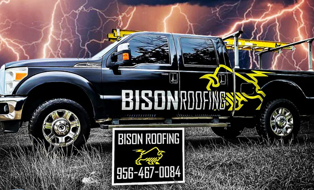 A black truck branded with the "Bison Roofing" logo stands in a field beneath a stormy sky, with lightning illuminating the scene. The truck's door prominently displays the distinctive yellow bison logo. A sign featuring the same logo is positioned in the foreground, encouraging you to call 956-467-0084.