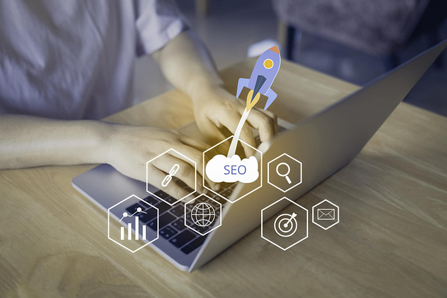 A person types on a laptop, surrounded by SEO icons—a rocket and magnifying glass—capturing the essence of an SEO crash course in under 5 minutes. The setting is a casual indoor environment with a wooden table, embodying quick and effective learning.