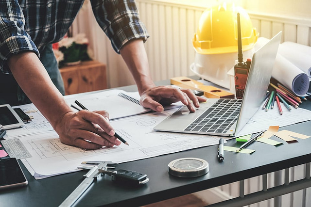 Male architects or engineers write a draft of the construction project on the blueprint; how will seo benefit my roofing company