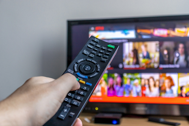 A hand grips a remote control aimed at a television, where the screen showcases a vibrant streaming service interface complete with colorful thumbnails and a progress bar. This scene underscores the transition from traditional media marketing to dynamic digital content exploration.