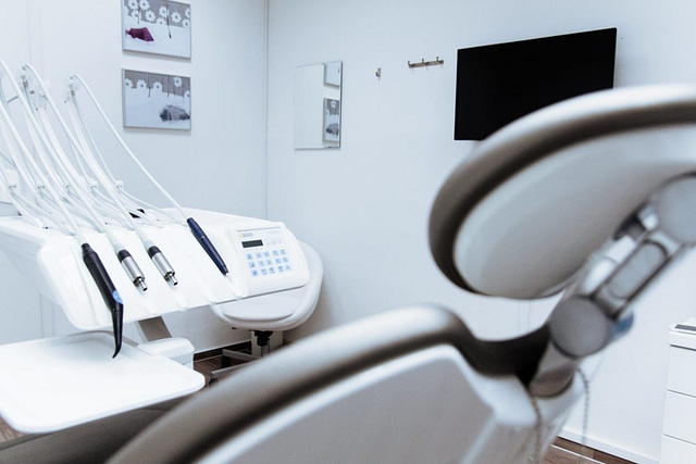 Experience modern dentistry at Dynamite Dentistry, where cutting-edge technology meets contemporary design. Our clinic features a sleek dental chair and state-of-the-art equipment in a bright room with white walls, abstract art, and a flat-screen TV for enhanced comfort.