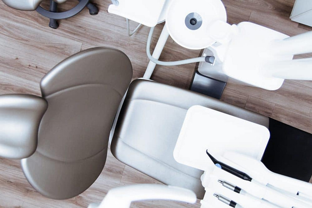 An aerial view of a modern dental clinic reveals an efficiently arranged dentist's chair and equipment, exemplifying effective dentistry practices. Strategically placed tools and lighting on a wood-patterned floor create an inviting atmosphere for patients, subtly enhancing lead generation.