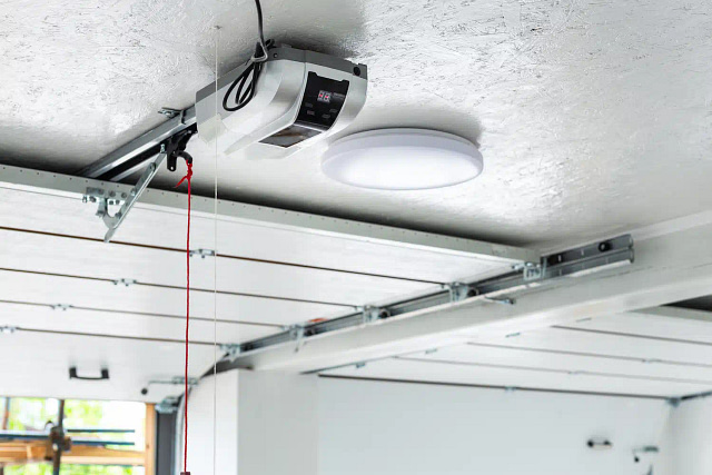 Showcased in the garage is a state-of-the-art automatic garage door opener, accompanied by a circular LED light fixture. The visible tracks ensure seamless door operation, with a red emergency release cord for safety. This setup exemplifies sleek and efficient modern design, ideal for contemporary garage door marketing. best garage door ppc agencies