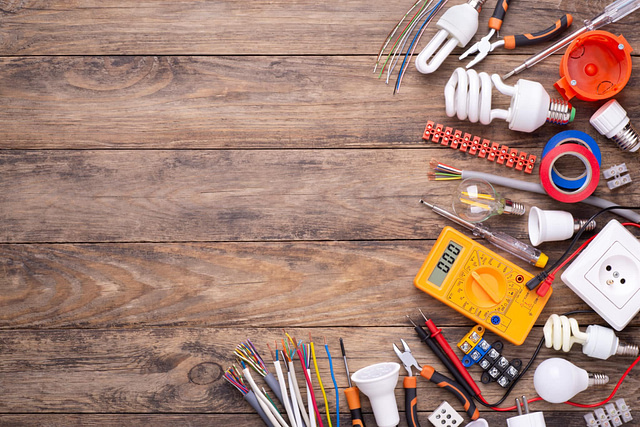 On the right side of a wooden surface lies a well-organized display of essential electrical tools and components—light bulbs, a multimeter, pliers, electrical tape, wires, and a power socket. This setup is ideal for electrician marketing visuals. The left side is intentionally kept clear for customizable use on Hook Agency's website.