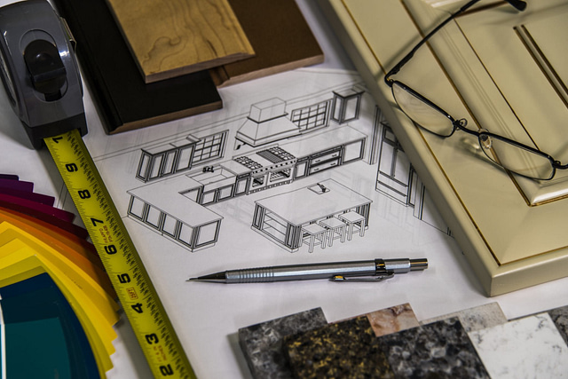 A kitchen design blueprint is complemented by an array of material samples, such as wood and stone textures, sparking innovative ideas. A measuring tape, pen, and glasses are strategically positioned atop the design, hinting at upcoming home remodeling and interior planning projects.
