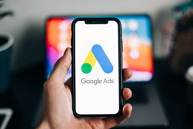 A contractor showcases a smartphone with the Google Ads logo prominently displayed, while a laptop in the background hints at lucrative digital marketing opportunities.