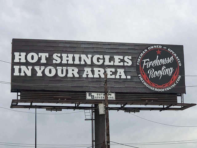 **Clever Billboard Design: "Hot Shingles In Your Area"**

Firehouse Roofing's creative billboard showcases the catchy slogan "Hot Shingles In Your Area," effectively using a roof shingle background for visual impact. The branding is reinforced with the logo positioned on the right. Notably, a power pole partly conceals this striking advertisement, adding an intriguing element to its presentation.