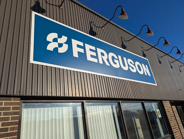 The image showcases the exterior of a Ferguson HVAC Distributor / supplier, distinguished by its prominent blue sign featuring an illuminated white logo. Renowned for outstanding customer service, Ferguson stands as a leader in HVAC distribution. The building combines brown corrugated siding with a brick facade, emphasizing its industry-leading status.