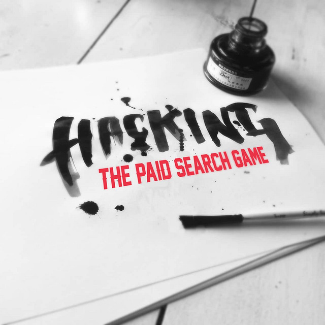 A brush and ink bottle lie beside a sheet of paper with the text "Hacking the Paid Search Game" written in bold, artistic lettering. Ink splatters decorate the monochrome background, hinting at innovative techniques in SEO and paid search strategies.