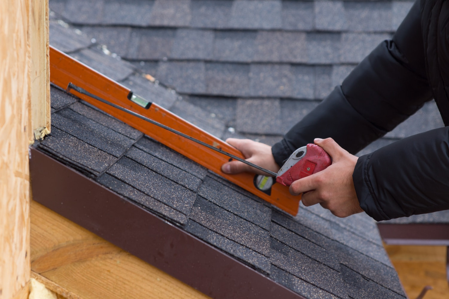 Roofer considers roof measurement software vs hand measuring while holding a tape measure