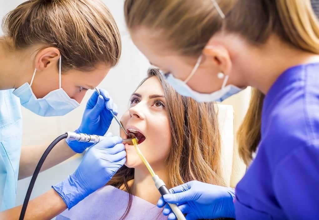 young woman getting dental procedure from two female dentists; types of dental insurance