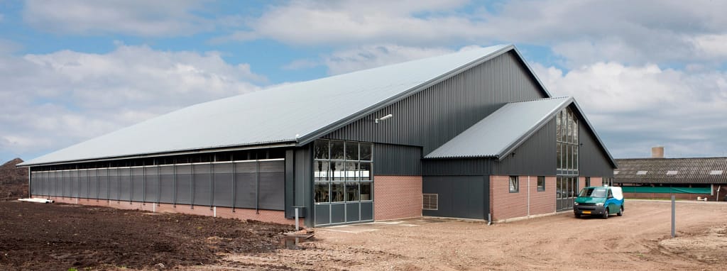 A large industrial warehouse with a gray metal roof and brick base, located in a rural area