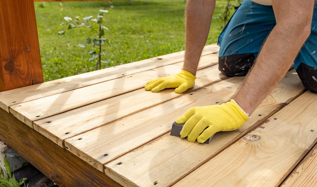 A person sands the wooden deck to create a smoother surface