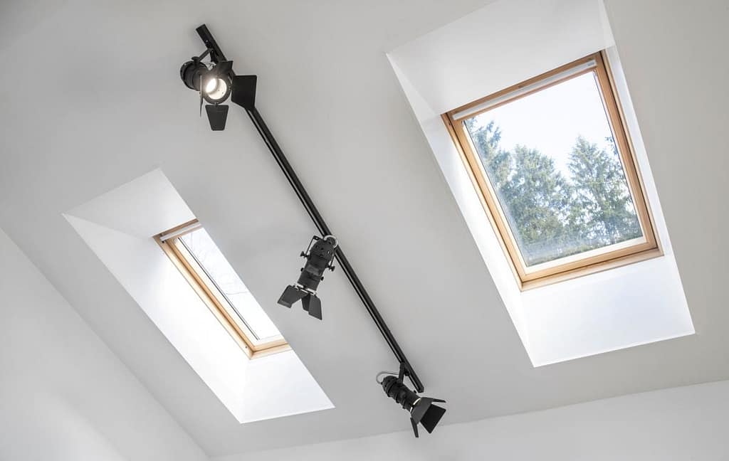 Three spotlights are mounted on a black rail near two skylights