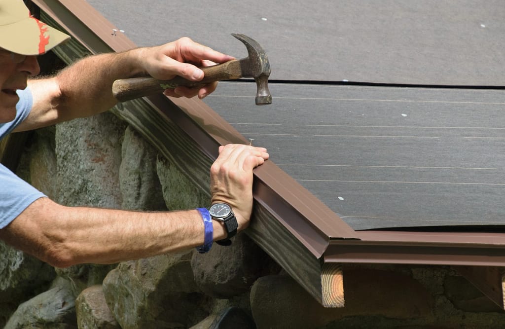 contractor repairs drip edge flashing using hammer after finding signs of a roof leak
