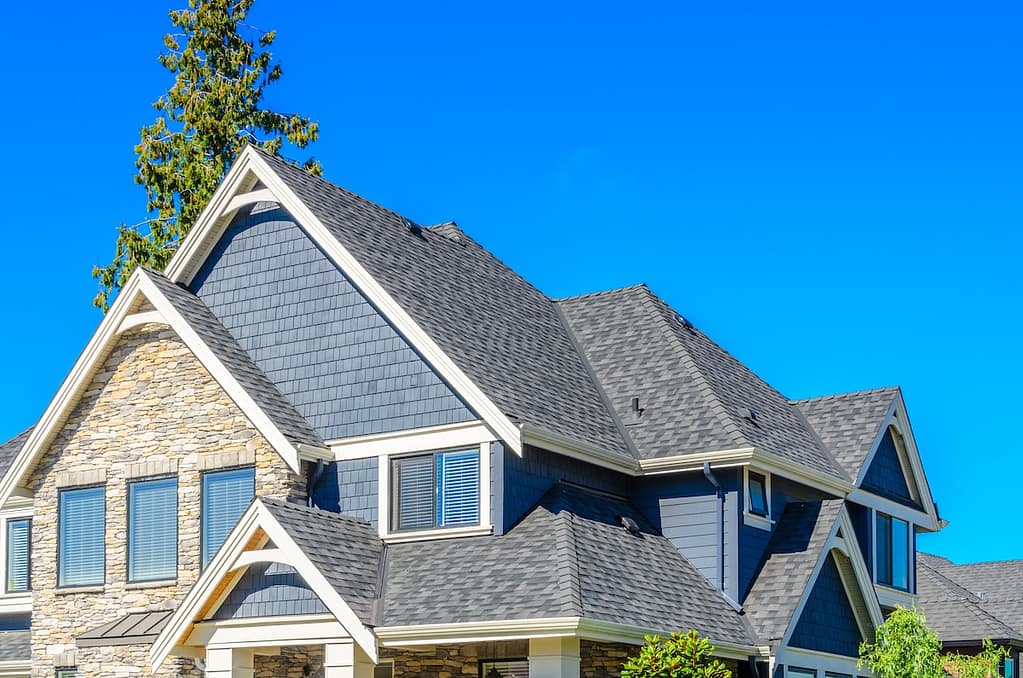 A two-story house with dark blue siding, gray roof shingles, stone accents, and white trim