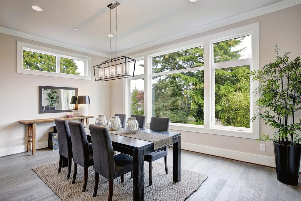 Luxurious modern dining room boasts a black dining table illuminated by a rectangular chandelier and surrounded by gray velvet dining chairs over taupe sisal rug finished with rustic console table.