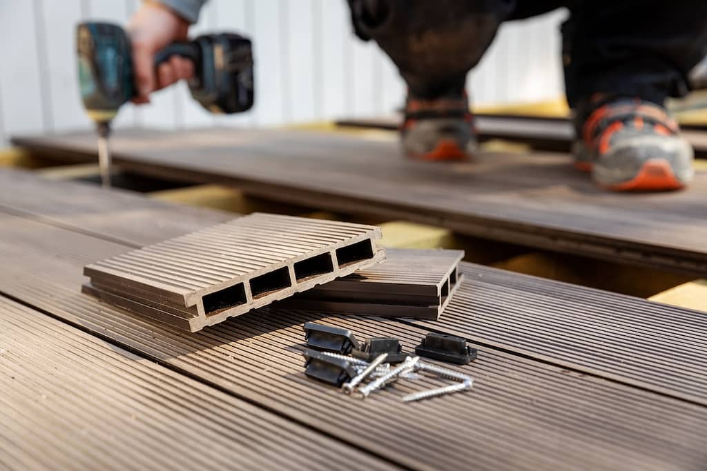 A person installs composite decking boards using a power drill