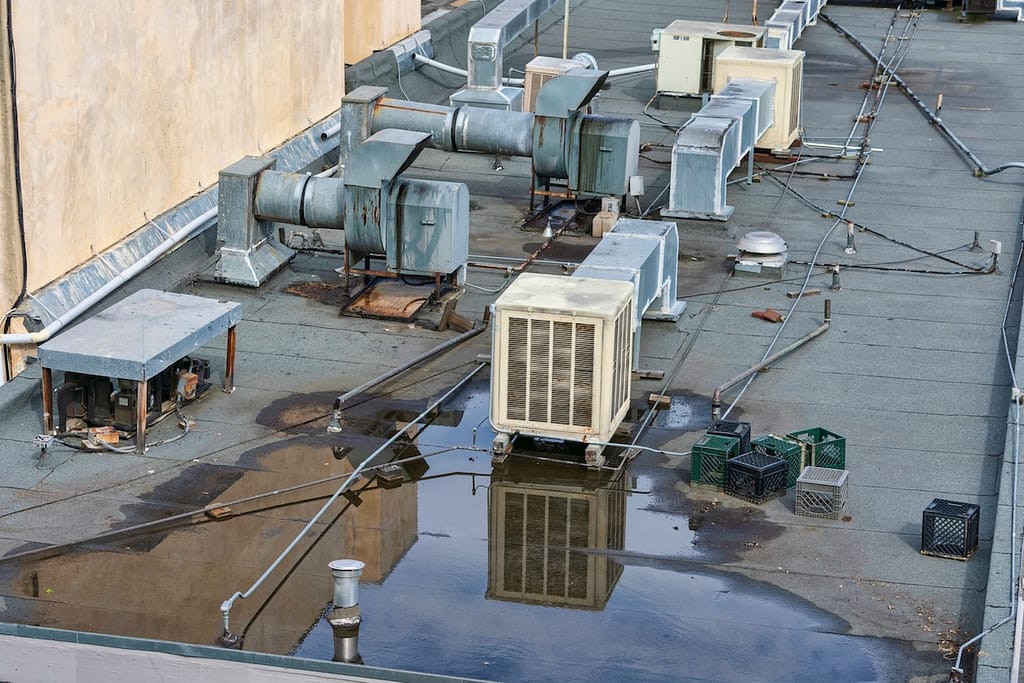 Several HVAC units and vents sit on a flat rooftop with a large puddle of water