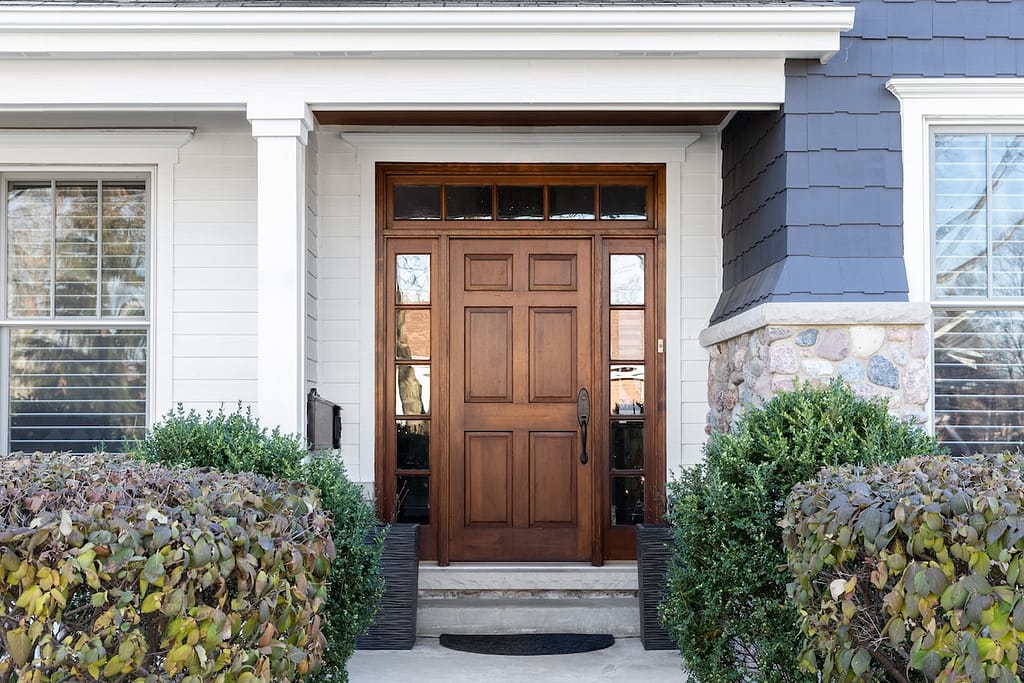 A wooden front door, surrounded by windows, with white, blue, and stone siding.