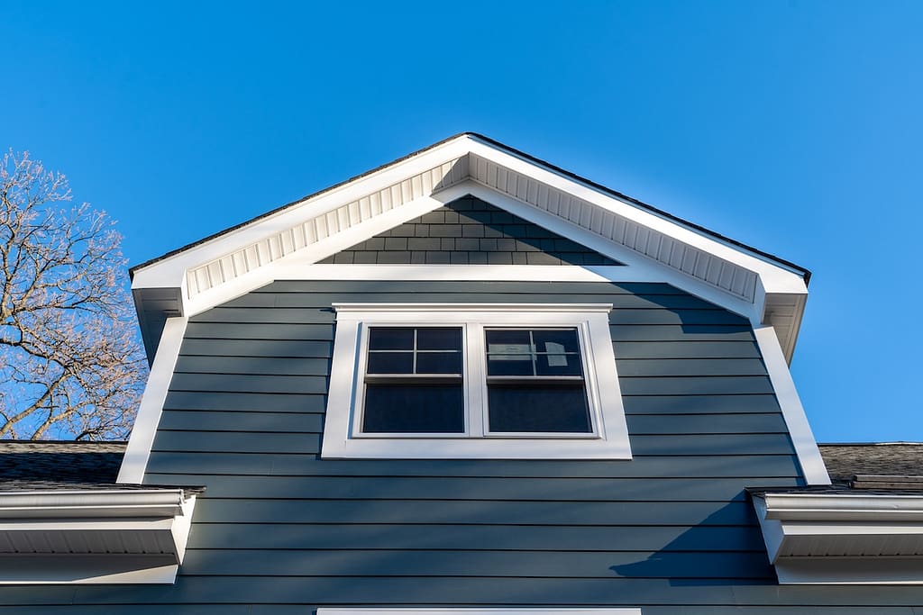 New restoration facade with double hung window w/ fixed top sash and bottom sash that slides up, divided by two white grilles, thick elegant frame, blue vinyl siding contrasting white corner, gable