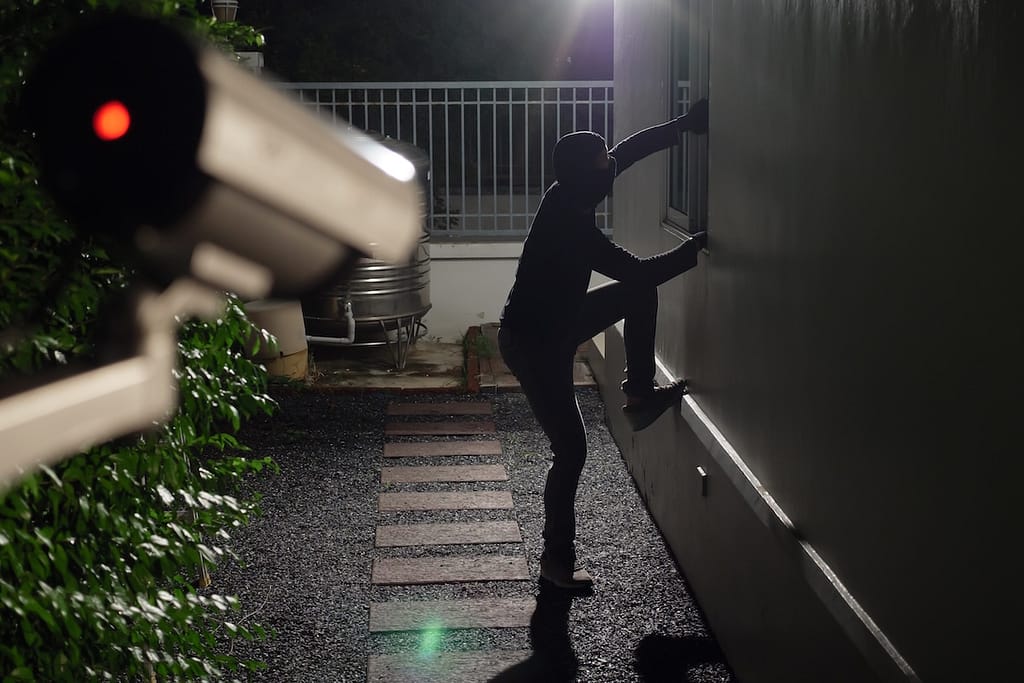 security windows Thief wearing black suit with balaclava and glove being caught by CCTV, surveillance camera during sneak into a house at night