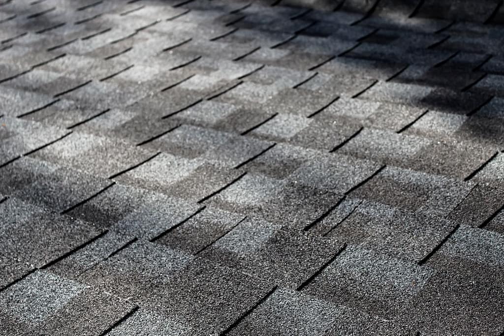 close-up of an asphalt shingle roof at an angle with dappled sunlight